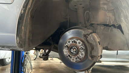 Car brake disc and suspension exposed in a repair shop, showing intricate mechanical details.