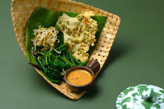 Pecel pincuk or Pecel Madiun on green background. Traditional food from Indonesia and Malaysia. Vegetables salad with peanut sauce, served with mungbean cracker.