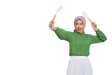 Cheerful beautiful Asian woman in green sweater and hijab hold spatula and spoon attack enemies while doing housework isolated on transparent background