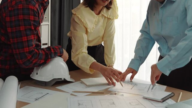 Smart architect and safety engineer discussion about building blueprint on table with architectural document, measurement tools and wooden block scatter around at modern office. Closeup. Delineation.