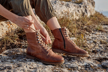 Woman tying boots on rocky hillside with ocean background travel adventure beauty nature scenery trip discovery wild exploration outdoor activity