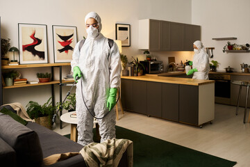 Worker disinfecting furniture with special equipment with his colleague in the room