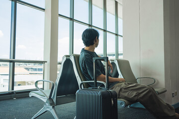 business concept with asian solo traveler wait for boarding time with luggage and seat in airport