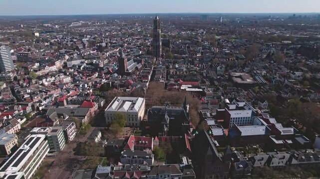 Panoramic aerial approach of De Dom medieval cathedral tower in scaffolding in Dutch city center of Utrecht towering over the cityscape against a blue sky sunrise and orange glow on the horizon