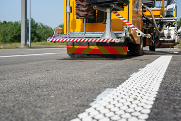 Close-up of white rumble strips on highway with road marking machine nearby during construction