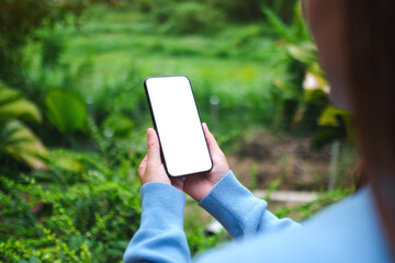 Mockup image of a woman holding mobile phone with blank white desktop screen in the nature outdoors