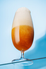 A tall glass of beer with a golden hue and frothy head, on a blue background