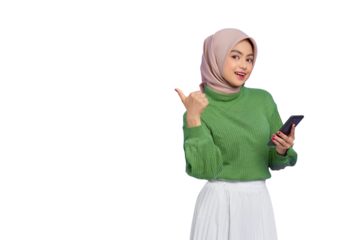 Portrait of smiling beautiful Asian woman in green sweater and hijab holding mobile phone and pointing finger aside isolated on transparent background