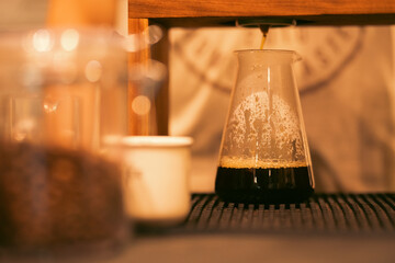 Freshly specialty brewed drip coffee pouring from ceramic filter into glass server with warm lighting atmosphere perfect for cafe menu design, barista lifestyle, morning beverage