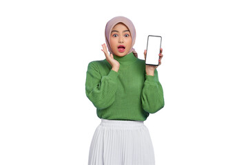 Excited beautiful Asian woman in green sweater and hijab showing blank screen mobile phone isolated over purple background