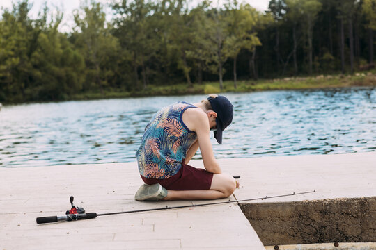 Young boy baiting fishing line on lakeside dock in summertime