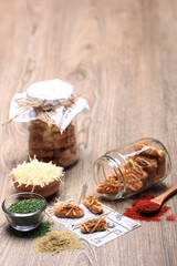 A vertical flat lay showcases savory cheese cookies, some on a decorative napkin, alongside ingredients like shredded cheese, dried herbs, and chili powder, with two jars of cookies 