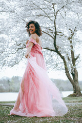Fototapeta premium A woman in a long pink dress against the background of cherry blossoms