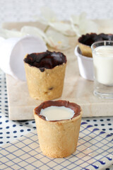 Two cookie cups filled with milk sit on a marble board with a glass of milk in the background
