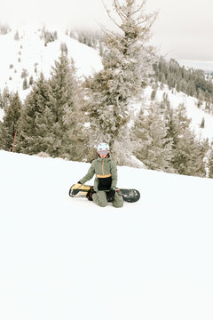 Young snowboarder kneeling, resting on snowy slope