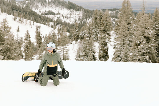 Smiling boy kneels with snowboard in snowy forest