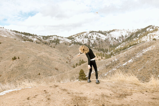 Teen boy throws rock in foothills under early spring sky