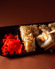 Chopsticks taking portion of sushi roll. Sushi rolls with salmon cream cheese and cucumber in take away package. Food delivery concept.