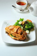 a plate of croissant sandwich with spicy meat filling and side salad