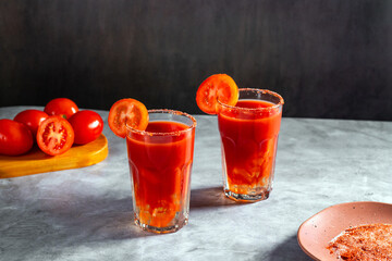 Two Bloody Mary cocktails in glass served with tomato slice and salt on dark background. Red cocktail. Alternative taste. Dirty dump drink