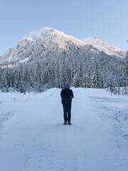 Hiker standing on snowy road looking at scenic snow covered mountain and forest