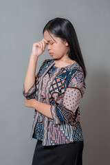 Young Asian woman showing stress and frustration with eyes closed, touching her forehead with fingers while frowning, expressing headache or emotional fatigue in studio shot.