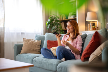 Obraz premium woman relaxes on sofa, watching her favorite show and snacking on popcorn. The scene radiates a sense of comfort and enjoyment, perfect for themes of downtime, entertainment, and cozy living.