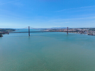 Drone view of 25 April Bridge spanning the water with Lisbon spread across the far bank
