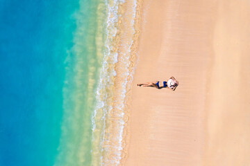 Aerial view of beautiful young woman in black swimsuit lying on sandy beach near blue sea with waves at sunset Summer vacation at Andaman Island	