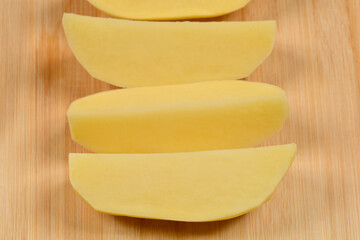 Several peeled and sliced potato wedges are arranged on a light brown wooden cutting board