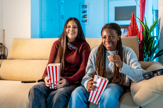 Smiling teen friends enjoying movie night with popcorn at home - Powered by Adobe