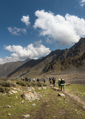 Fototapeta premium A group of hikers walking on the trail in the valley of Tien Shan maintains in Kyrgyzstan on a sunny summer day