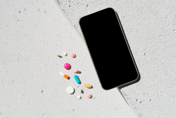 Mobile phone with blank screen and colorful vitamin pills on neutral concrete background with aesthetic sunlight shadow. Minimal healthy lifestyle concept