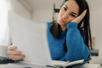 Stressed young woman reading documents at home office desk