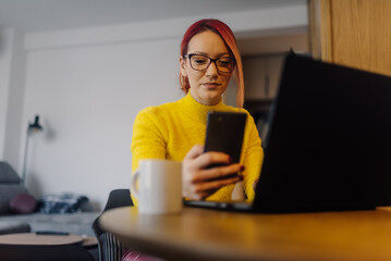 Focused freelancer working remotely from home using laptop and smartphone