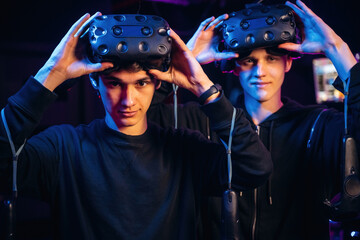 Taking off the eyewear. Two young men in virtual reality glasses indoors