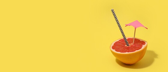 Half of fresh grapefruit with decorative umbrella and straw on yellow background with space for text