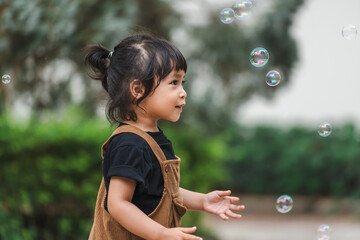 toddler girl playing soap bubble in park