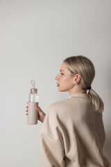 Blond young woman holding reusable plastic bottle with water in it. Healthy lifestyle and body care concept.