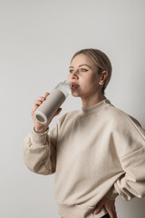 Blond young woman holding reusable plastic bottle and drinking water from it. Healthy lifestyle and body care concept.