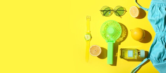 Composition with portable electric fan, fresh lemons and female beach accessories on yellow background with space for text
