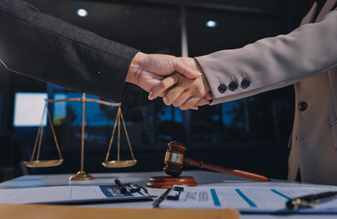 Two businesspeople are shaking hands in a law office with a scale and a gavel on the table.