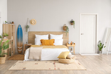 Interior of light bedroom with surfboard, houseplants and shelving unit