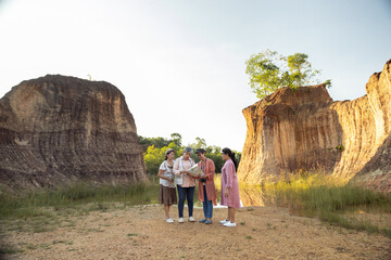 Four Asian senior women standing outdoors together at rocky cliff area holding map discussing travel route exploring scenic destination during relaxing afternoon adventure under soft natural light.