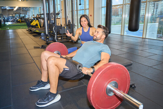 Personal trainer assisting client with barbell exercise