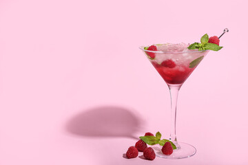 Glass of fresh raspberry mojito on pink background