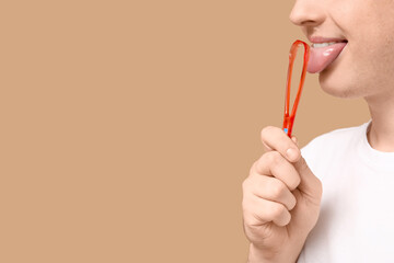 Man using tongue scraper on beige background, closeup
