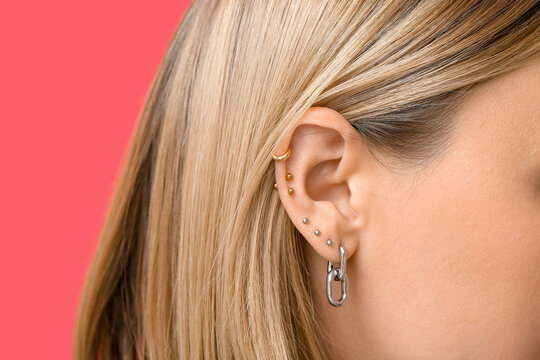 Woman with multiple ear piercing on red background, closeup