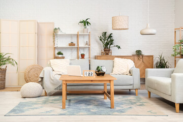 Obraz premium Stylish interior of beautiful living room with comfortable sofas, houseplants, shelving units and table with laptop