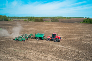 Obraz premium A red tractor is actively tilling a large, flat agricultural field